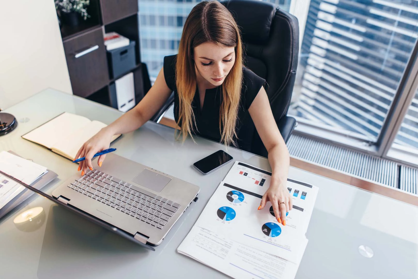 A businesswoman sits at a desk examining charts