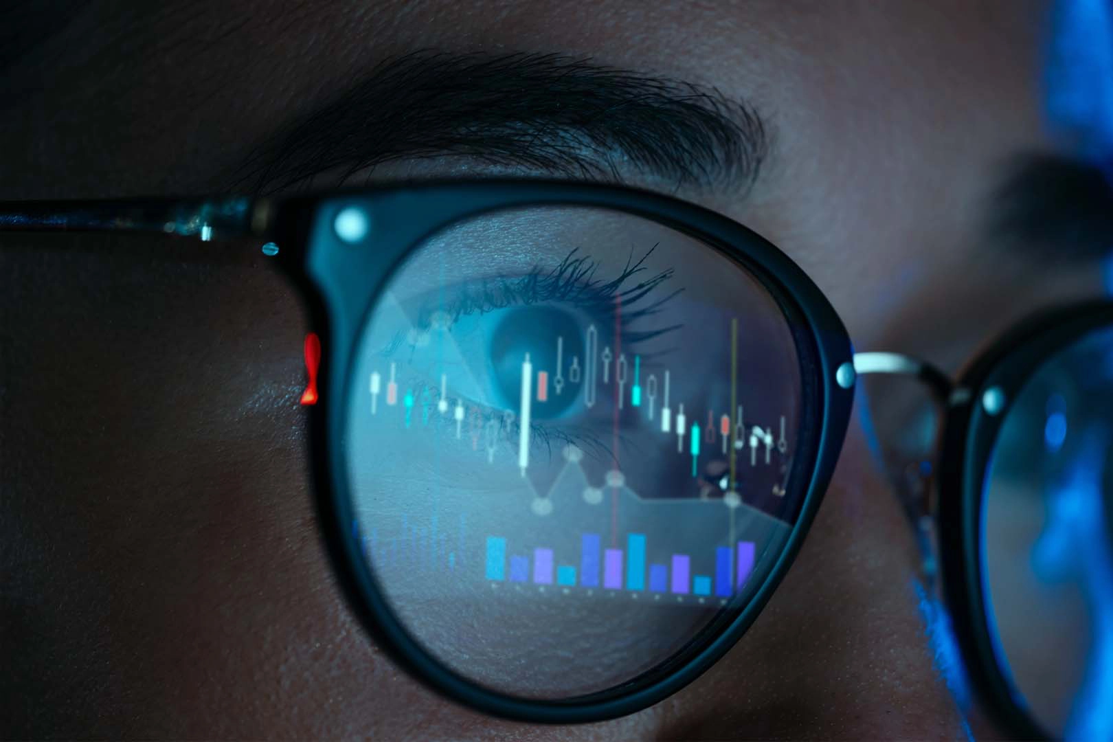 Close up of a woman wearing glasses with graphs reflected in the lense